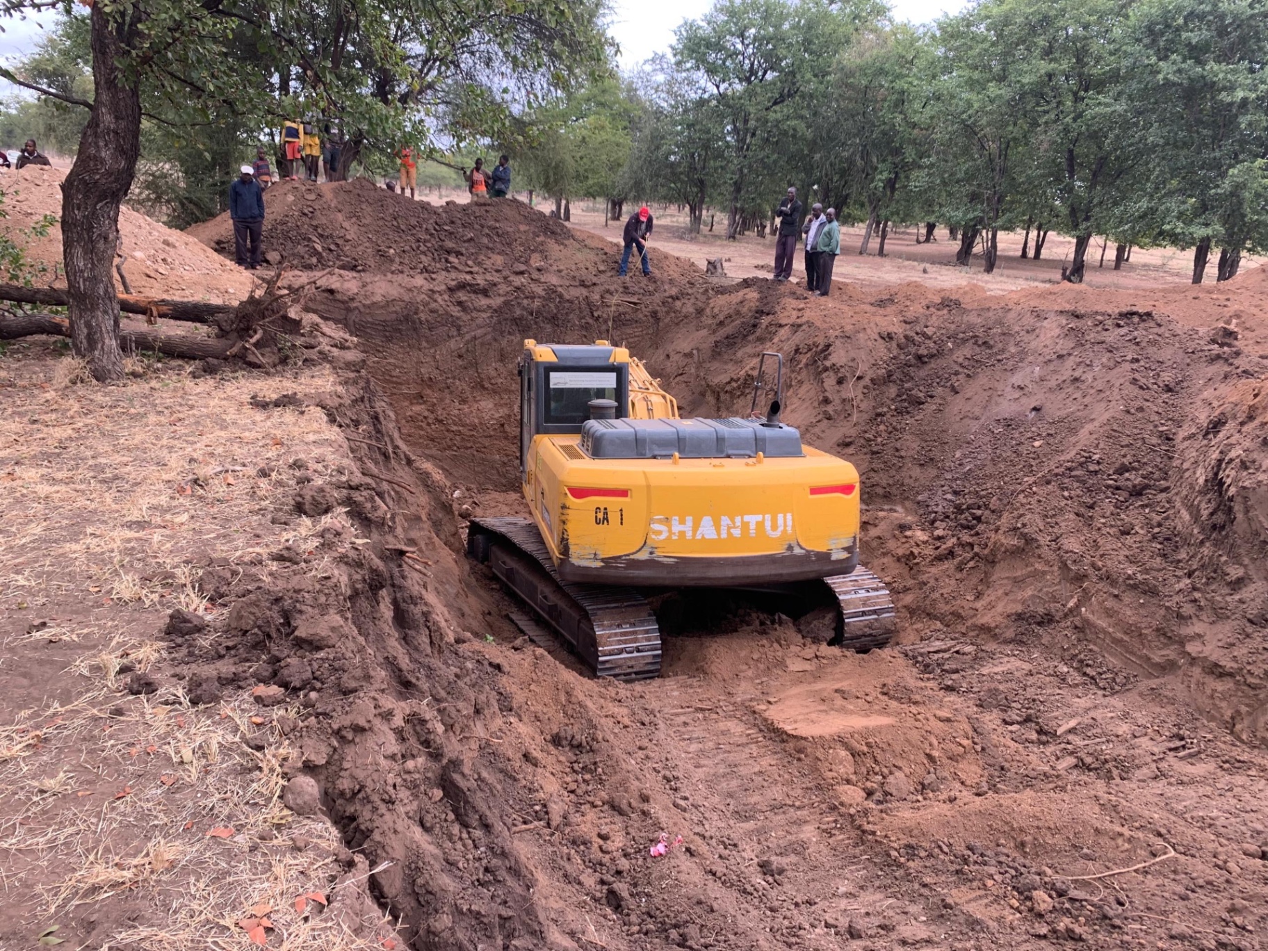 Shantui excavator digging a deep trench through red soil