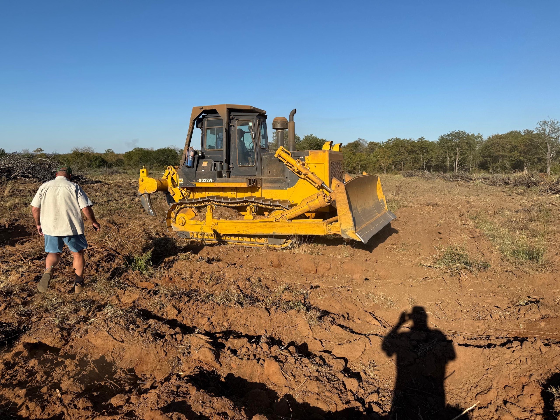 Shantui SD22W bulldozer on a bush-clearing site with piles of cleared brush