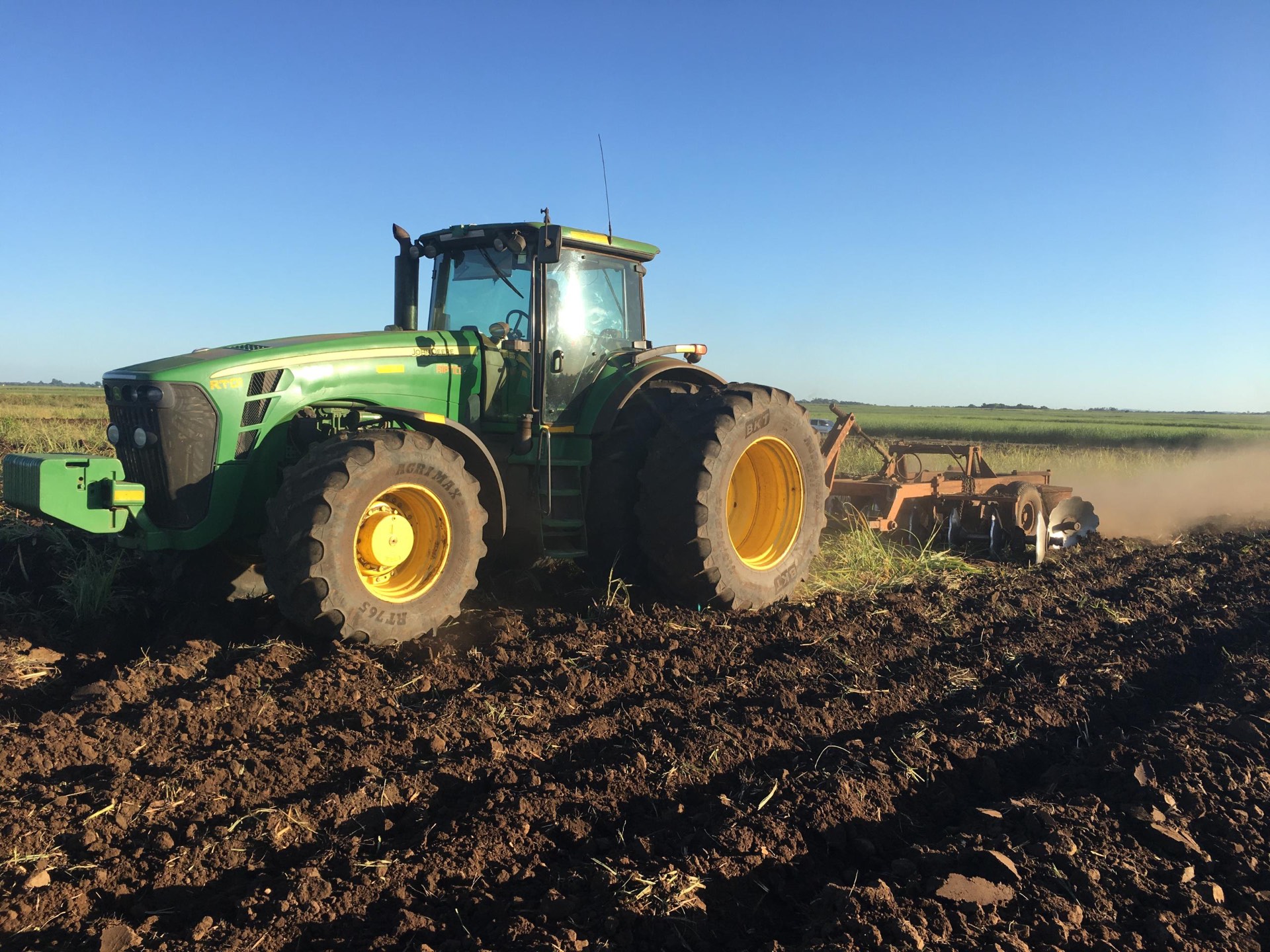 John Deere tractor with a heavy disc harrow working dark soil at sunset