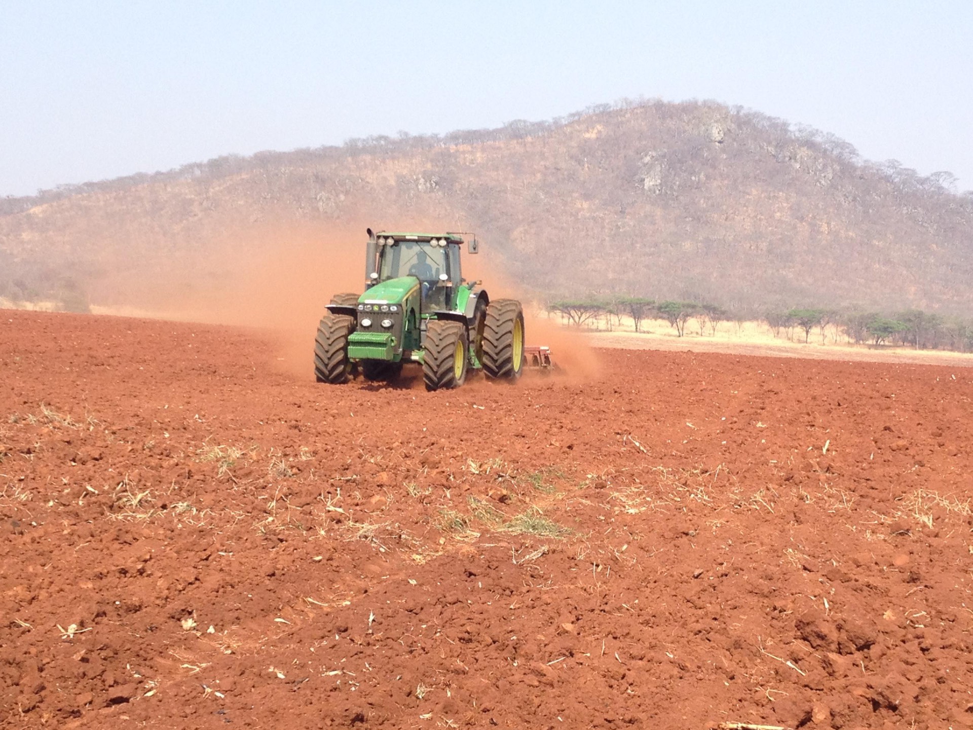 John Deere tractor heavy discing red soil with a hill behind