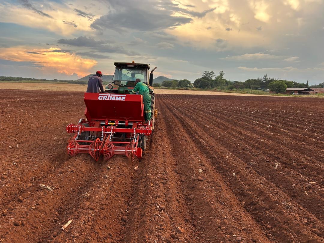 John Deere tractor pulling a Grimme planter through red soil at sunset